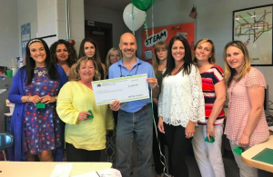 A man holding a check and balloons surrounded by ladies and everyone is smiling