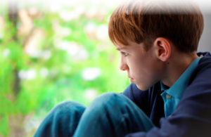 A young boy, sitting down and looking out into the distance with a look of despair