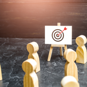 Wooden figurines facing a target board, symbolizing focus on goals and achievement. A dart hits the bullseye.