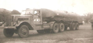 Black and white image of a vintage military tank truck with a driver and prominent star insignia on the door, parked on grass.